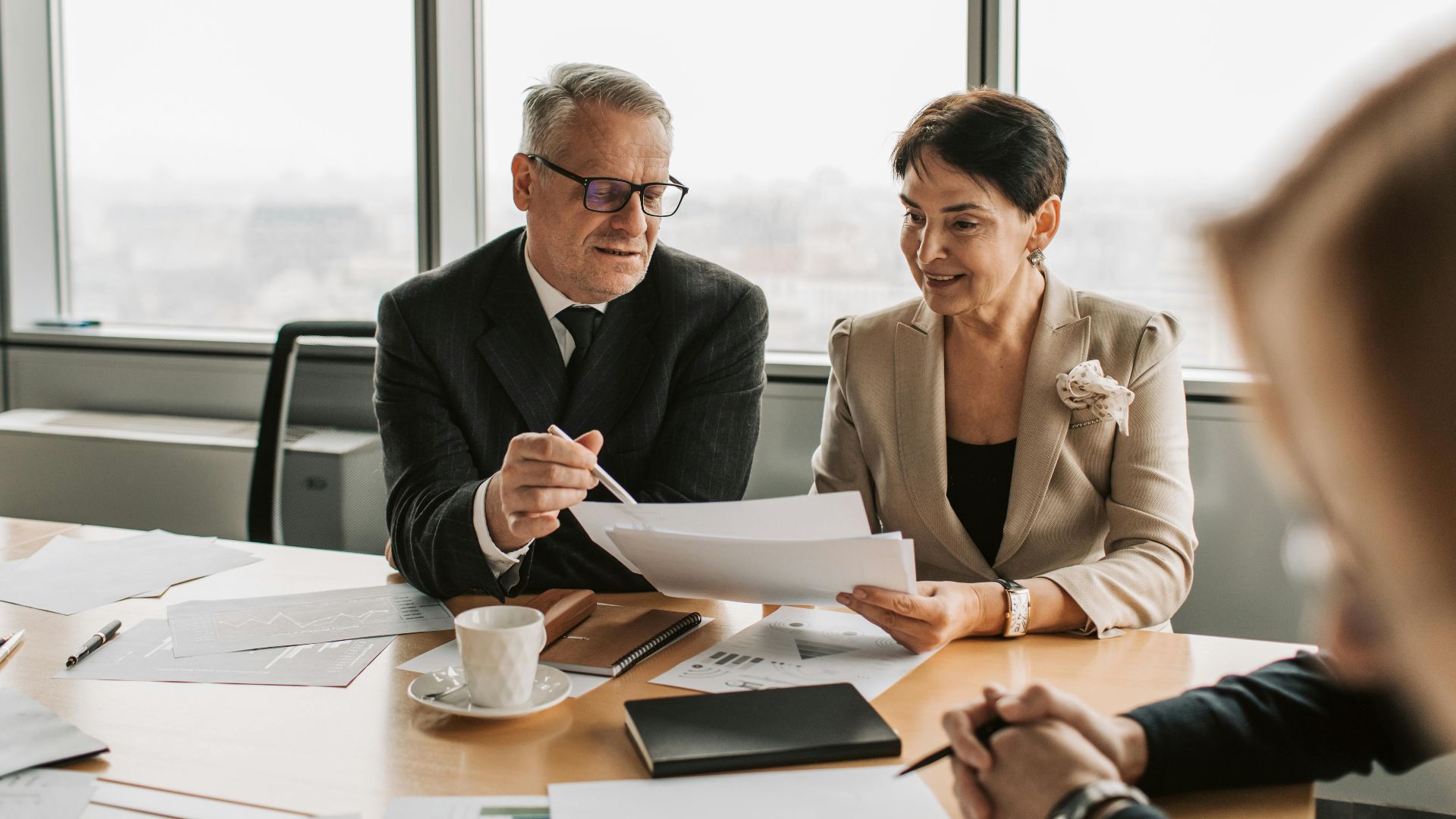 Senior business professionals discussing documents in a corporate office setting.