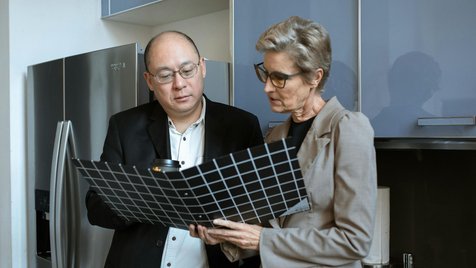 Two business professionals review documents in a modern office kitchen setting.