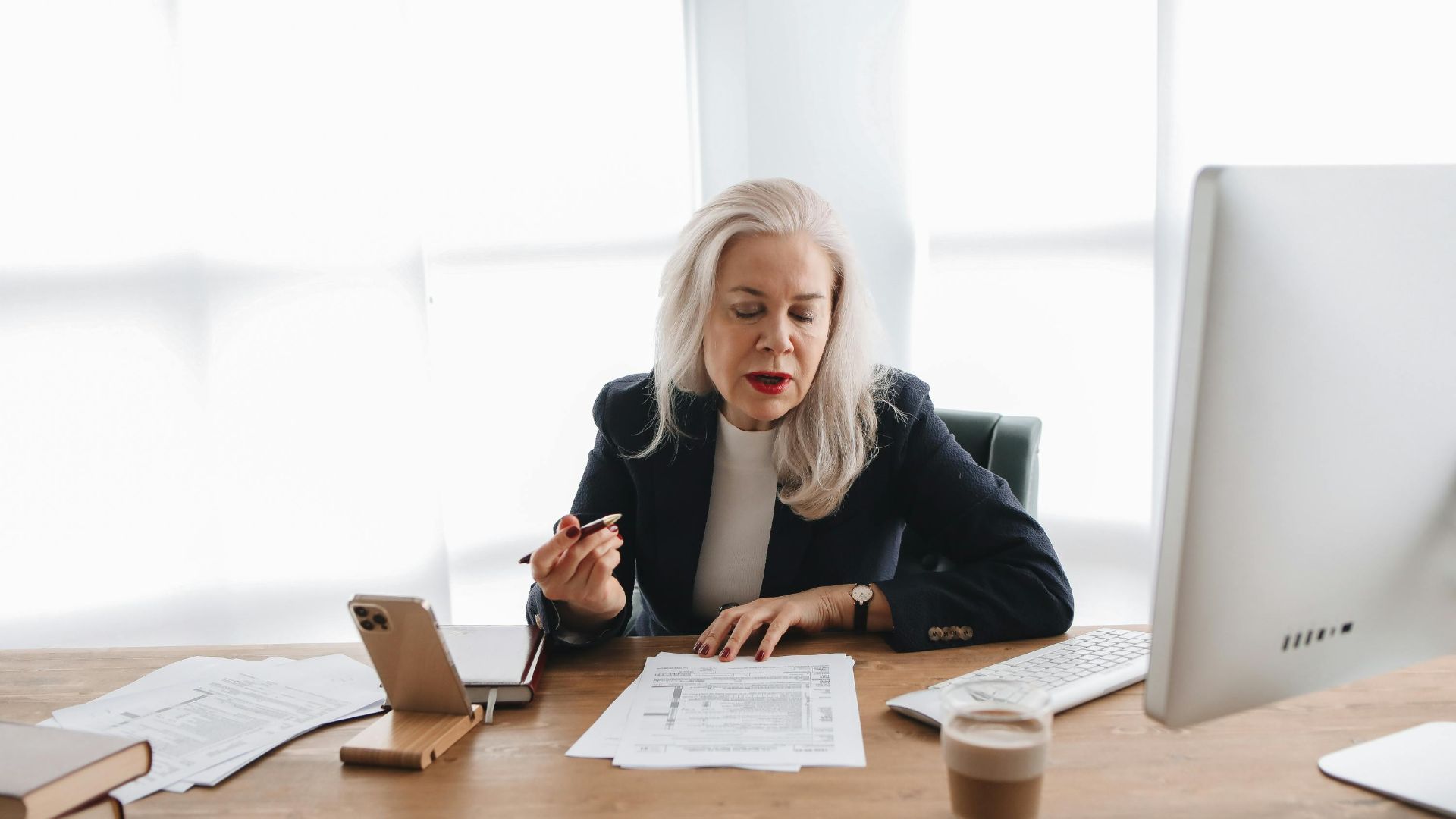 Senior woman in office reviewing financial documents with focused expression.