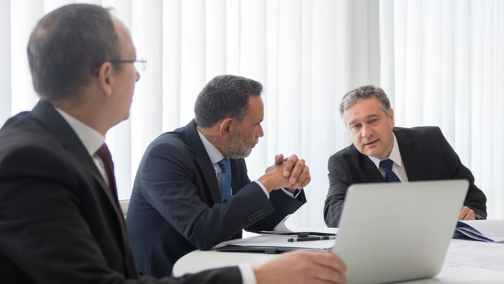 Three businessmen collaborating during a meeting around a laptop in a bright office.