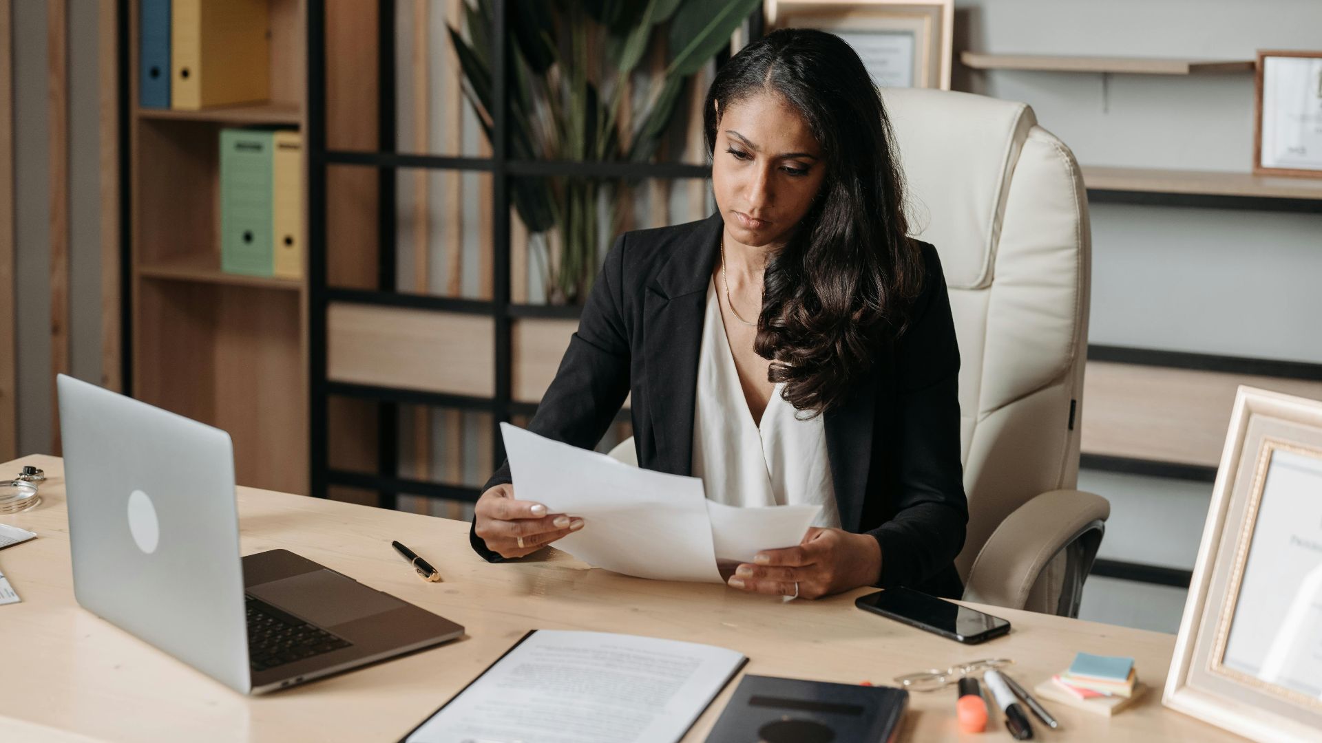 Business woman focused on paperwork at office desk, reviewing documents.
