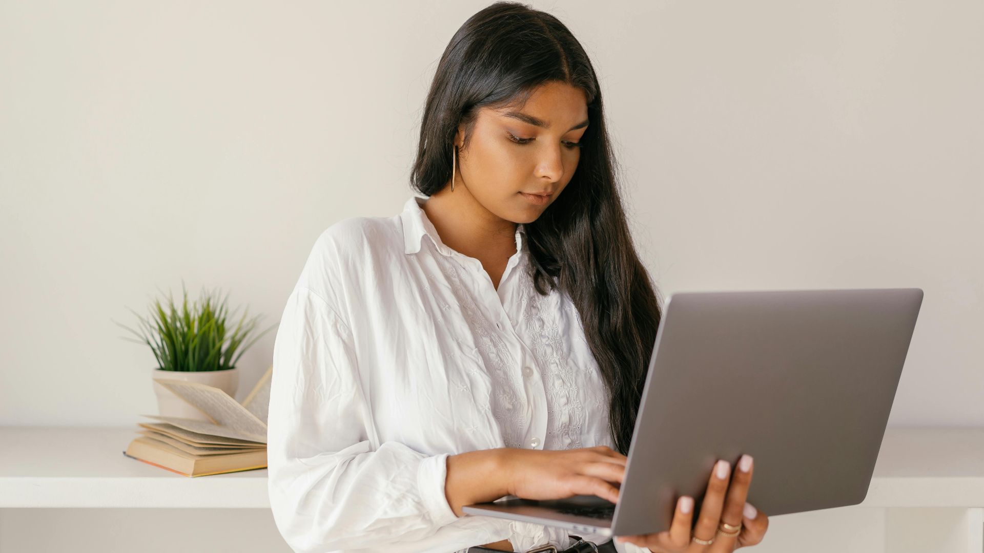 A young woman typing on a laptop while standing indoors, focused and professional.