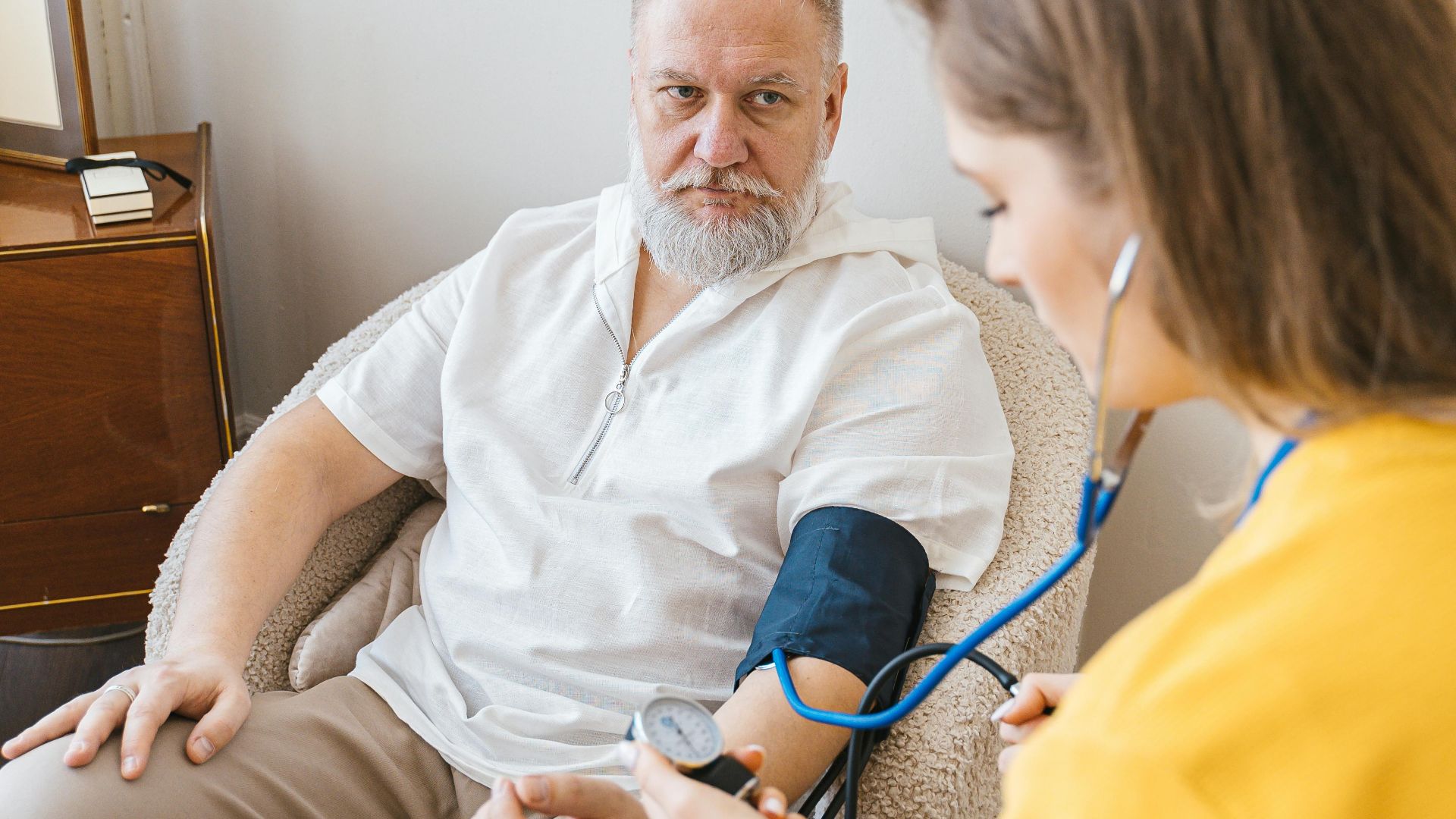 An elderly man having his blood pressure checked by a nurse during a routine health checkup indoors.