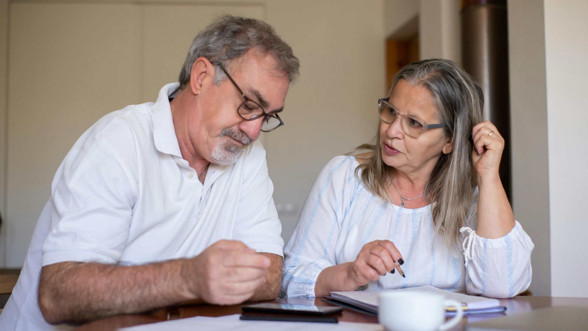 Senior couple reviewing documents and managing finances together at home, showing collaboration and care.