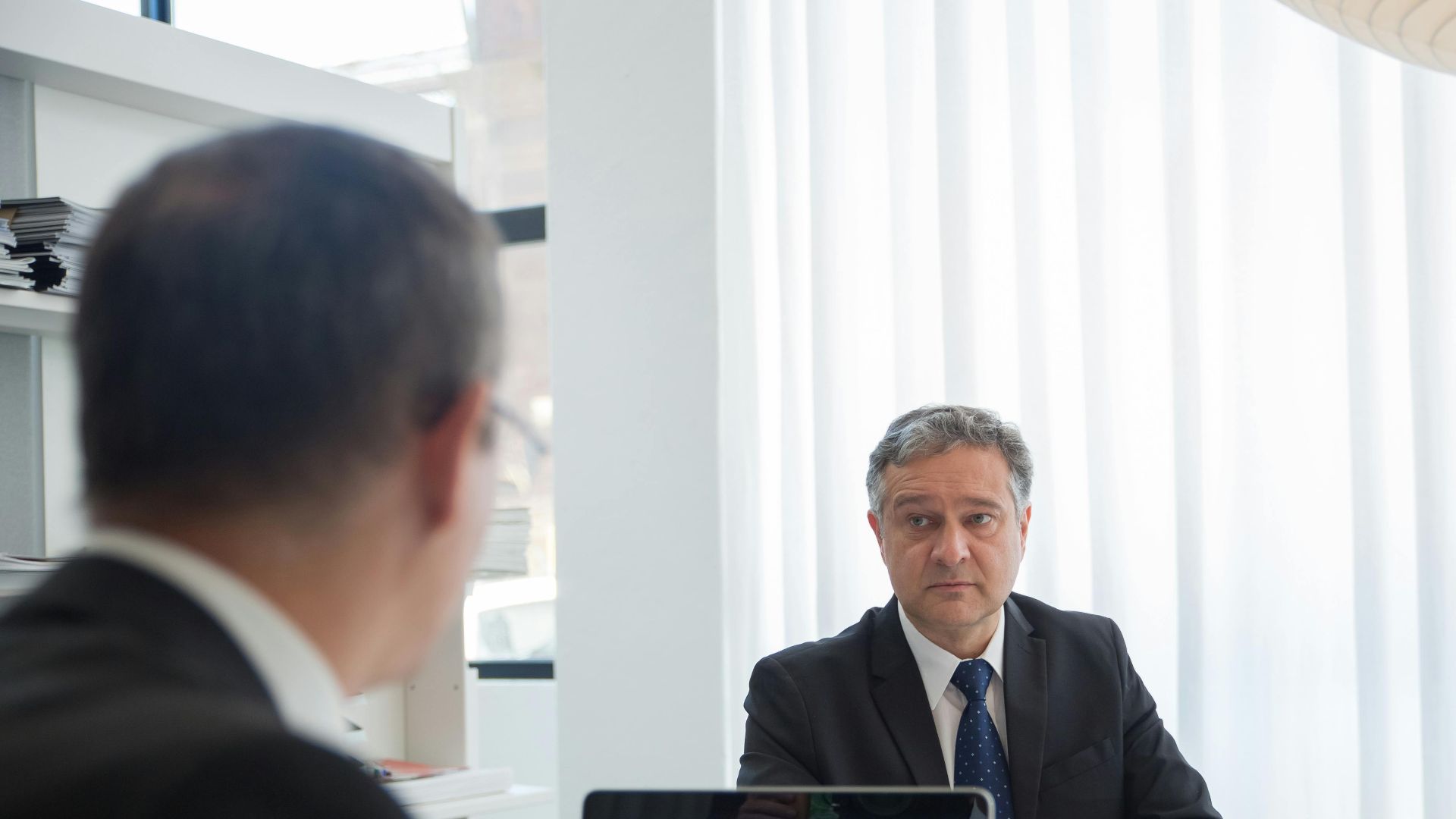 Two businessmen in discussion at an office desk with a laptop.