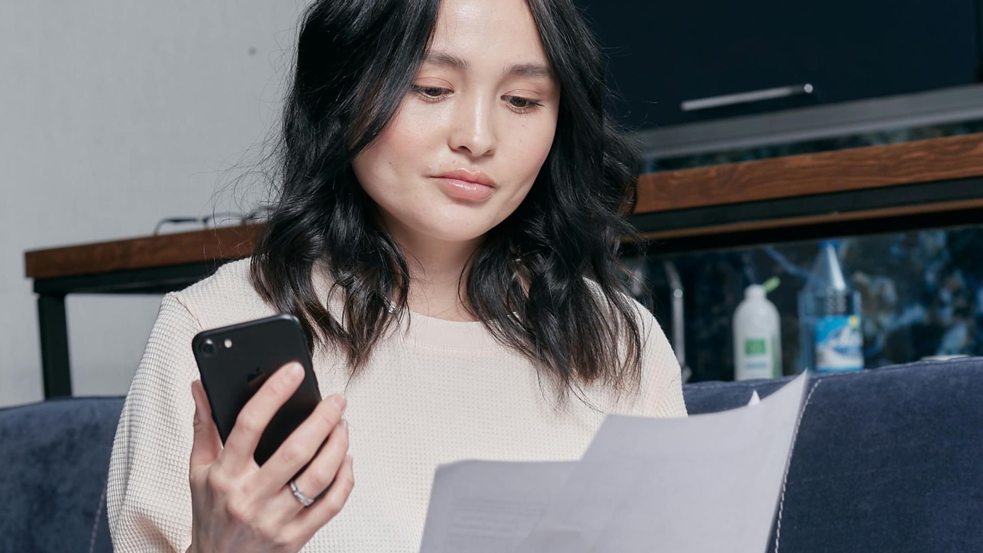 Young woman using phone and documents for home finance management.