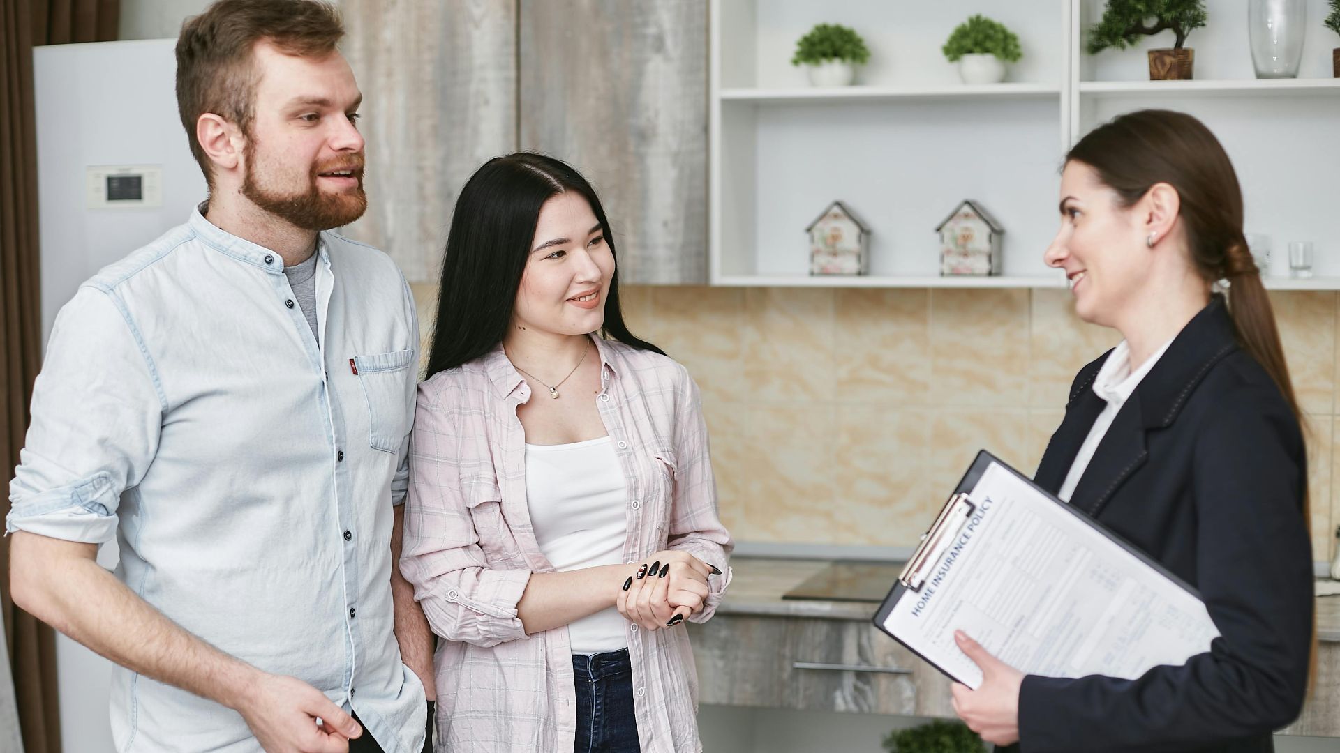 A young couple engaging in a conversation with a real estate agent inside a modern kitchen setting.