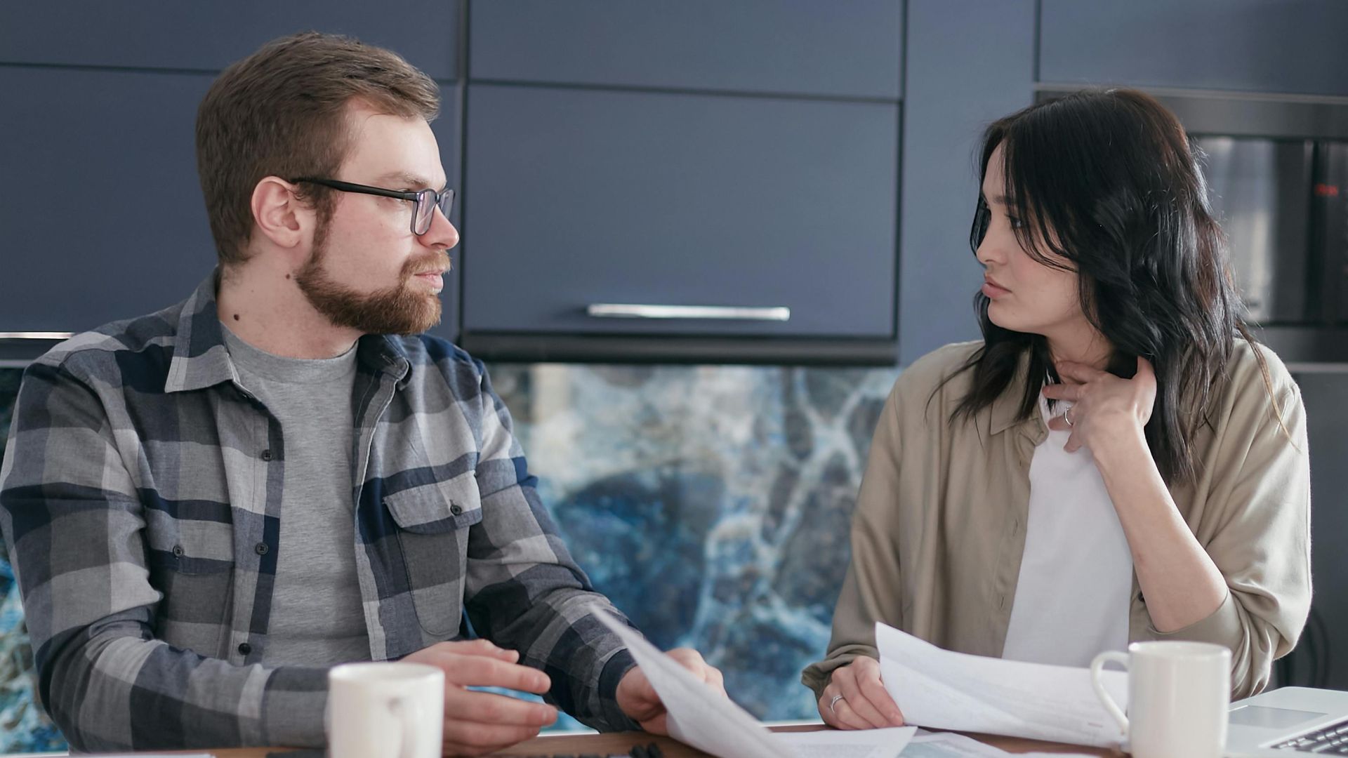 A young couple sitting at a table discussing bills and financial plans in a modern kitchen.