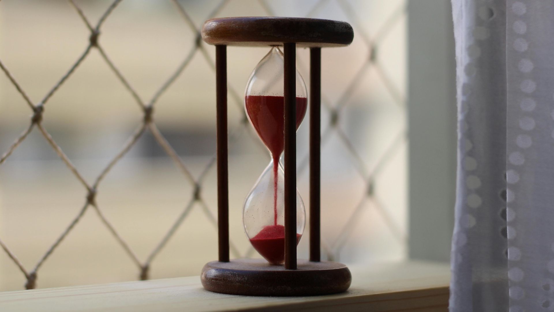 A close-up shot of a wooden hourglass on a window sill with gentle lighting, conveying a sense of time and tranquility.