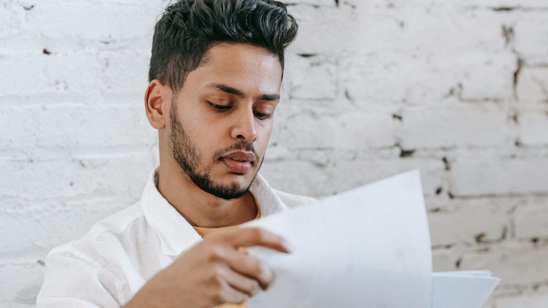 Concentrated young bearded Hispanic male sitting in armchair and analyzing contract while getting job offer