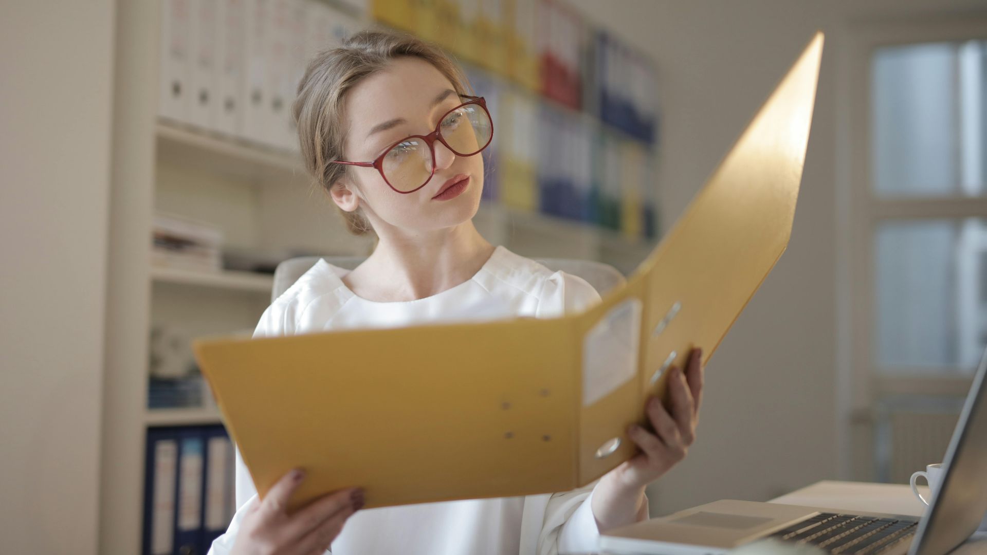 Caucasian woman intensely reading documents in an office setting.