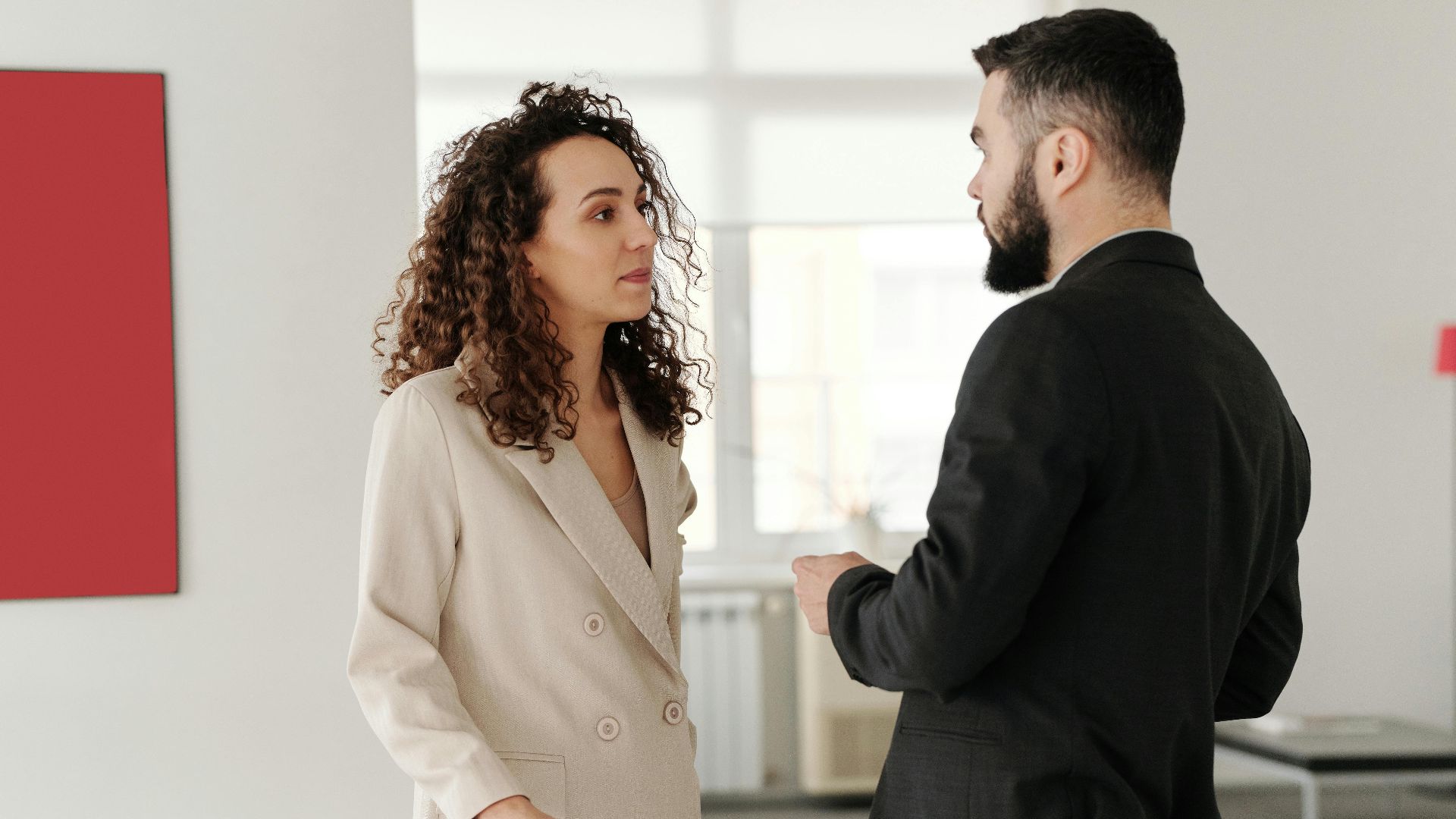 Two professionals engaged in a discussion in a bright, modern office setting.