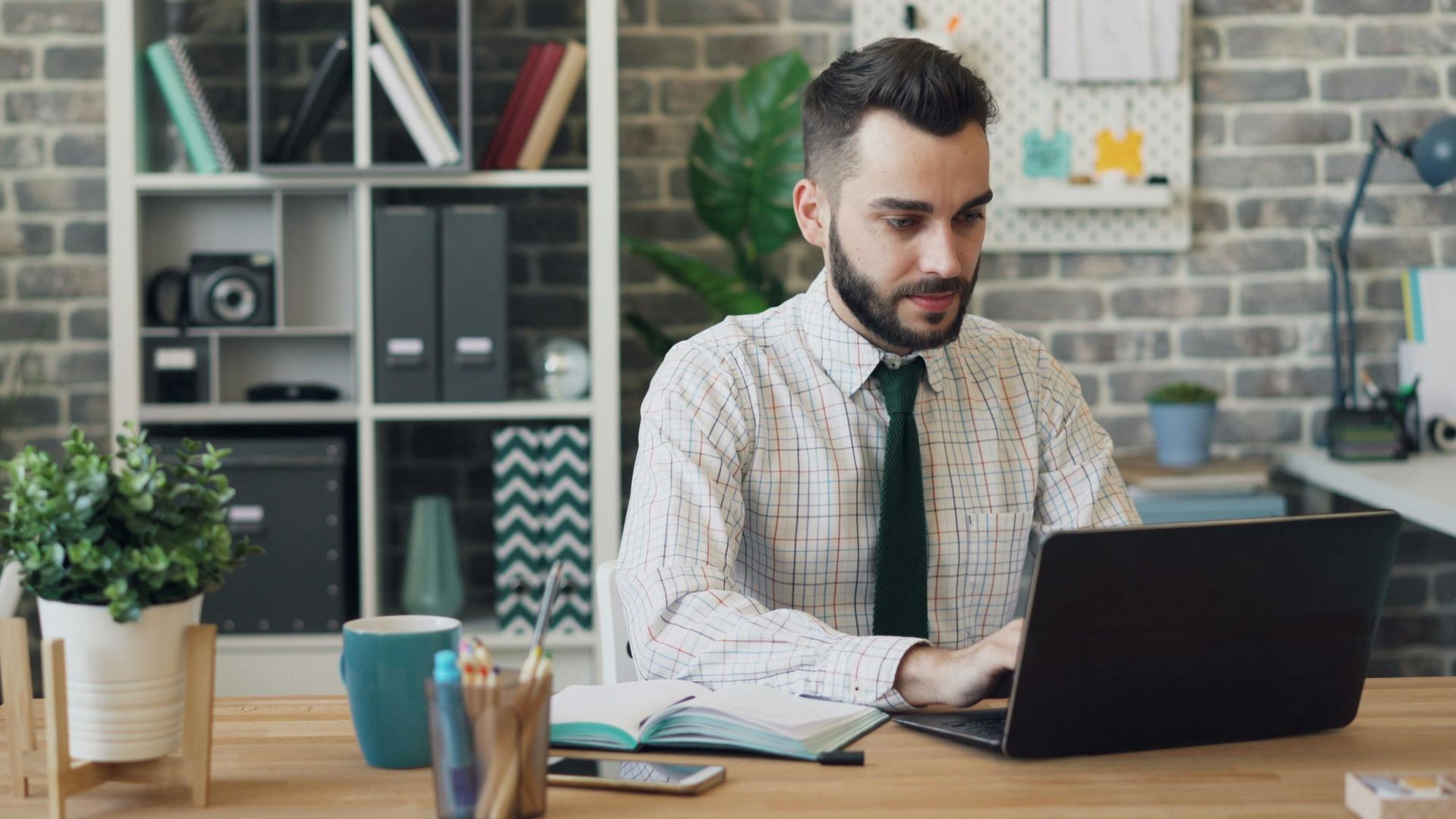 Man in a shirt and tie working on his laptop in a modern office setting.