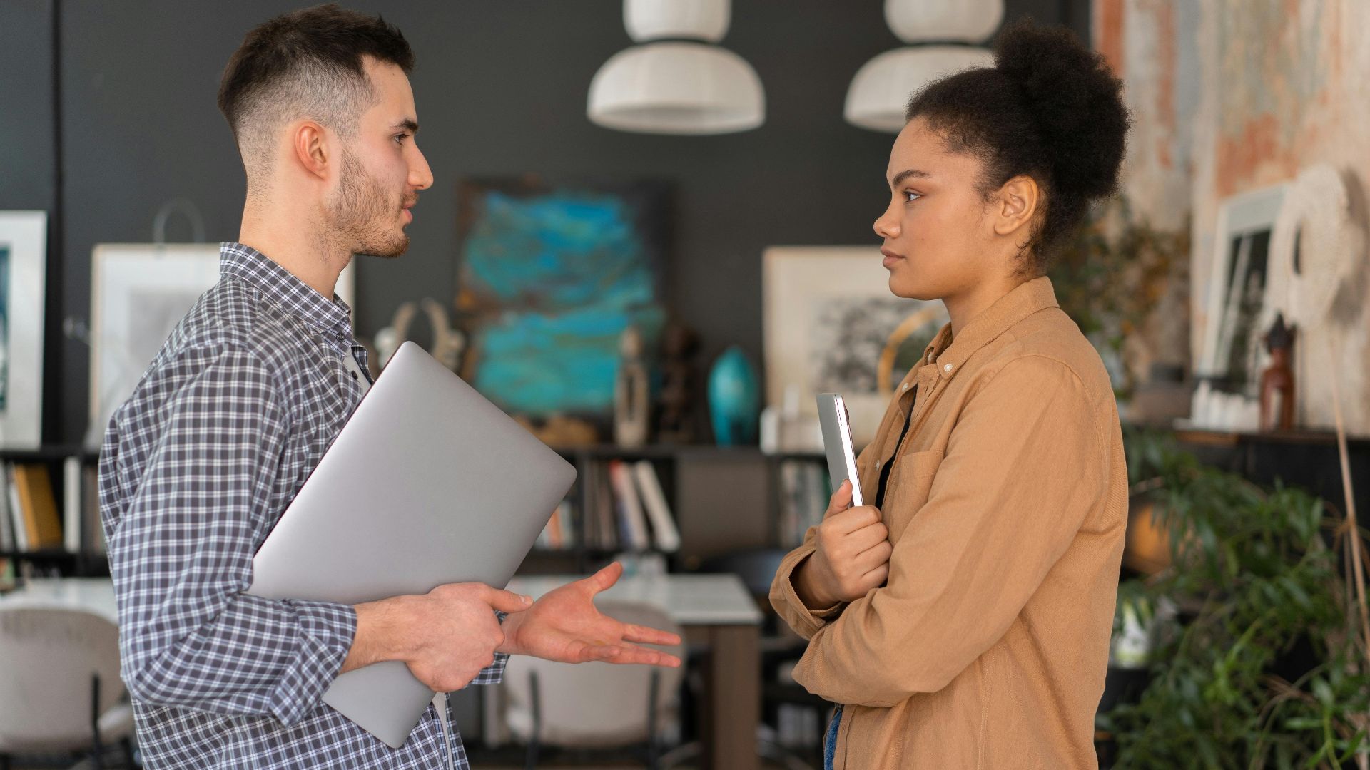 Two office workers engaged in a conversation, holding devices, in a modern office setting.