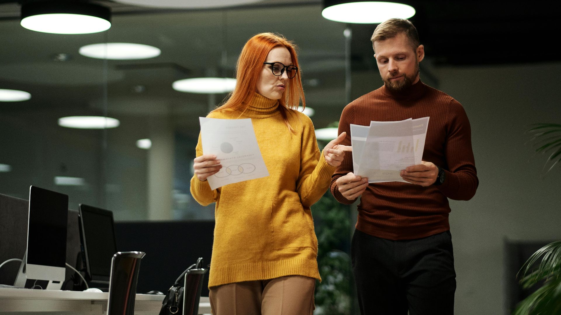 Two colleagues review documents while walking through a contemporary office space.
