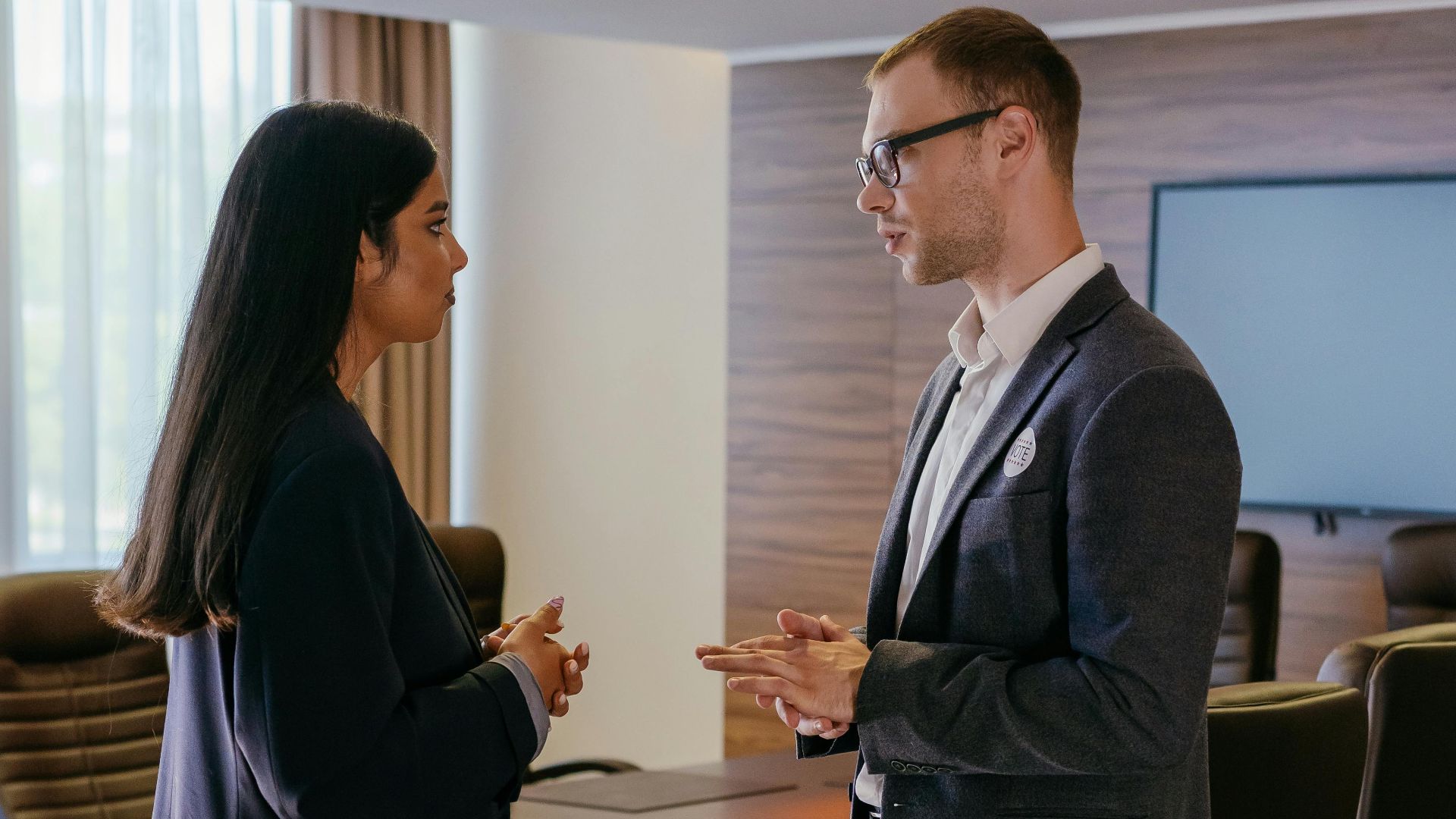 Two professionals engaged in discussion inside a modern conference room setting.
