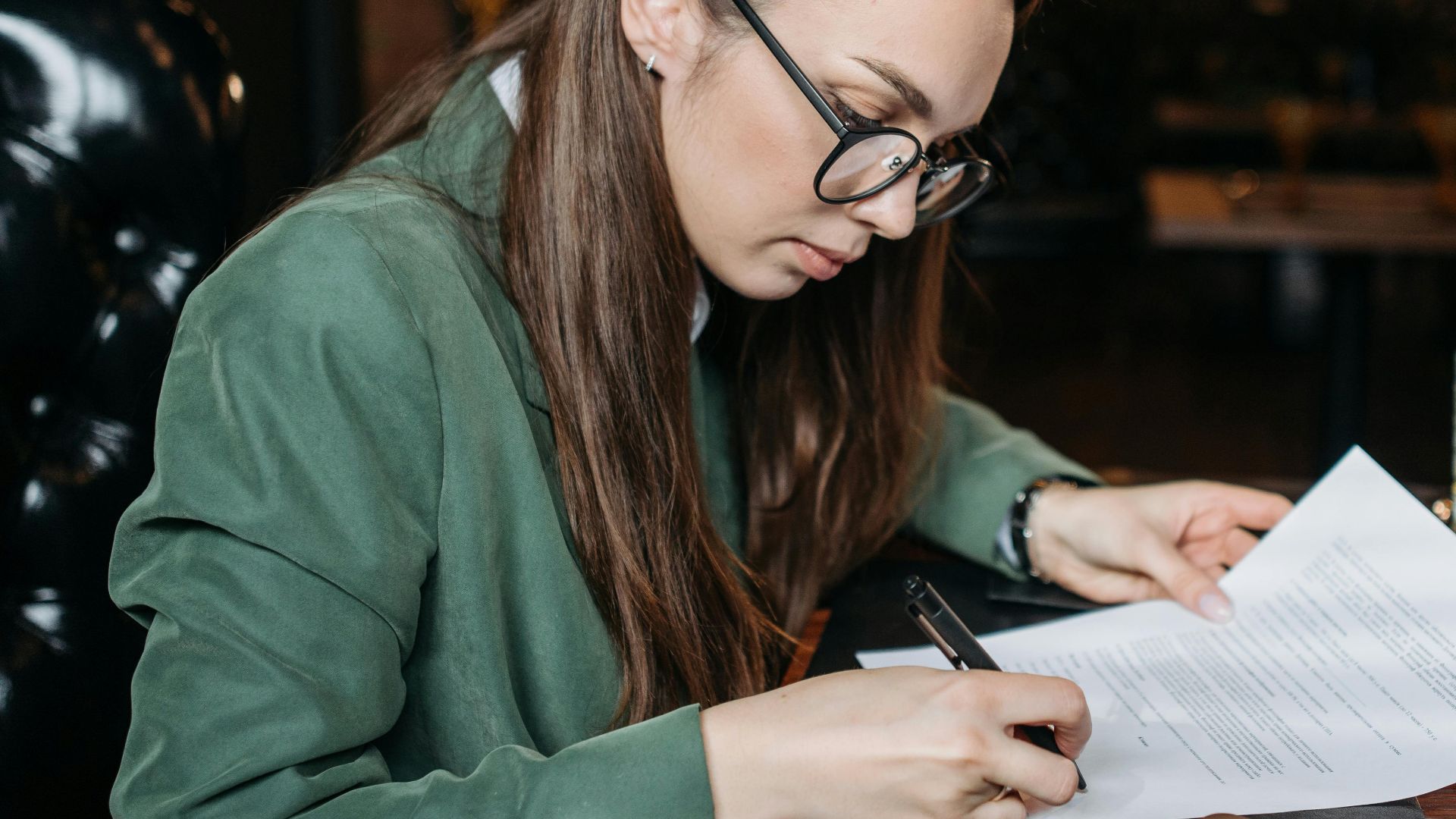 Focused businesswoman in green attire signing important documents at her desk.