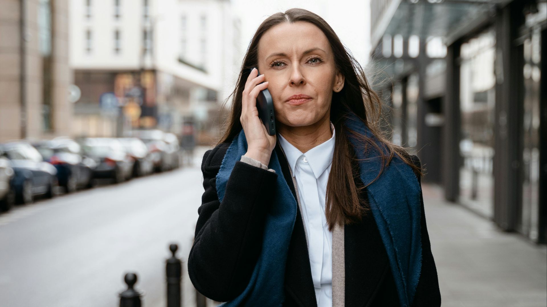 Professional woman walking in urban setting, engaged in cellphone conversation.