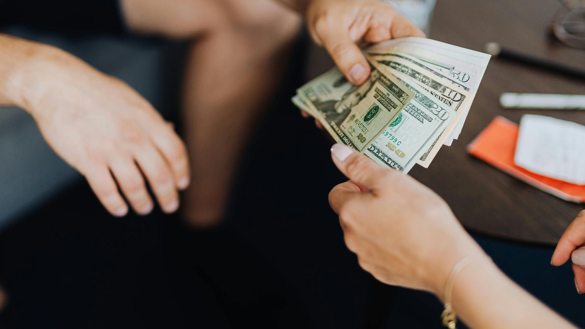 Close-up of hands exchanging US dollar bills, symbolizing a financial transaction or payment.
