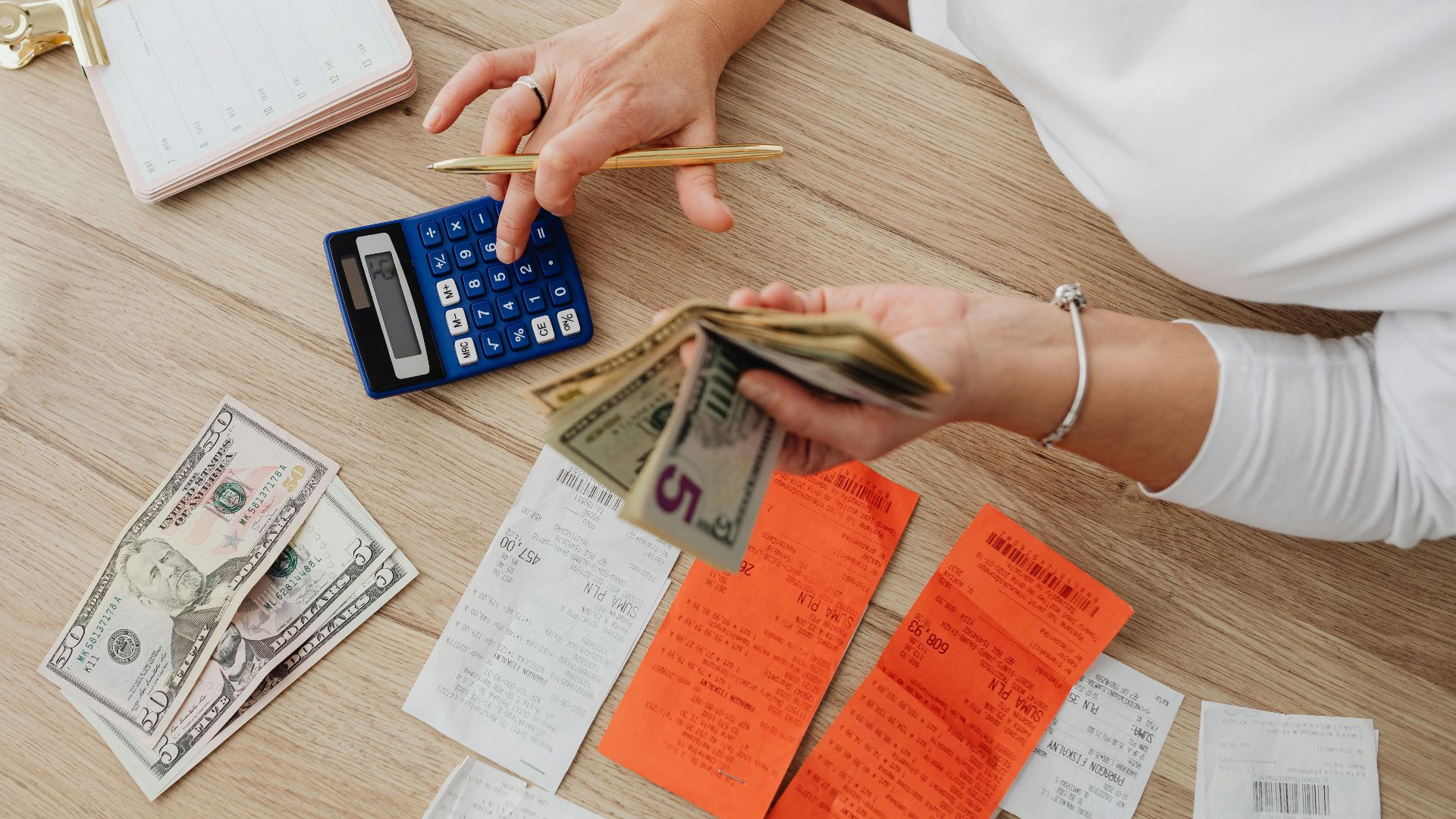 Overhead view of a person using a calculator to manage cash and receipts at a desk.