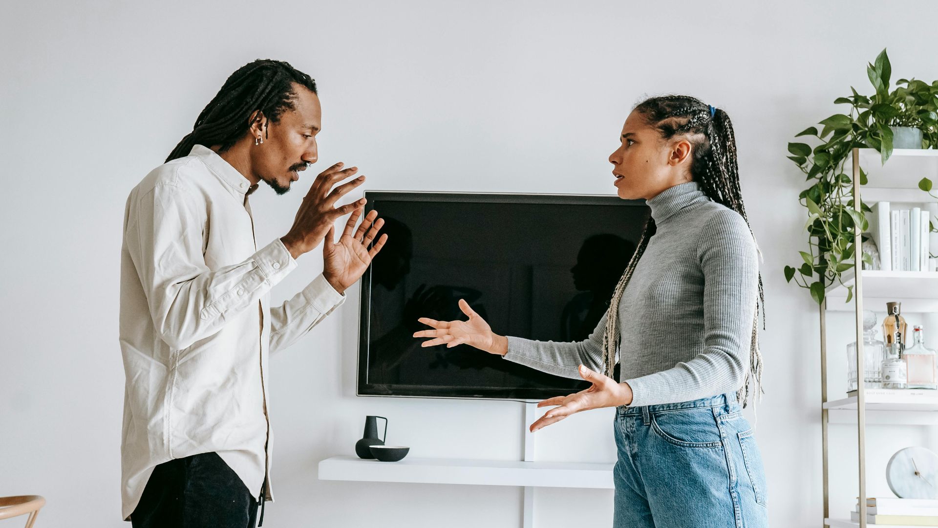 Side view of young African American female in casual outfit gesticulating expressively while arguing with frustrated husband in modern living room