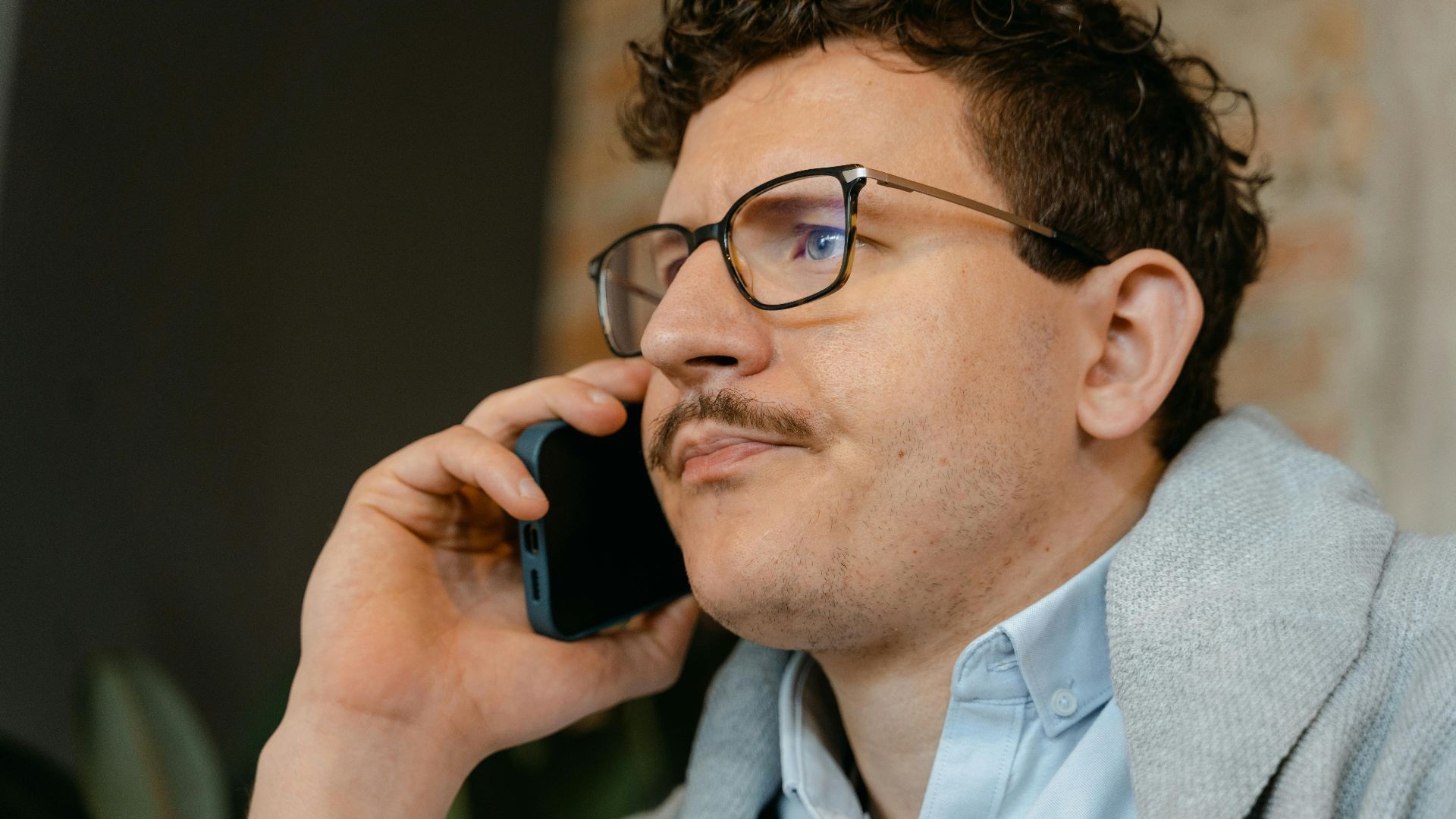 Man with glasses and mustache making a smartphone call indoors.