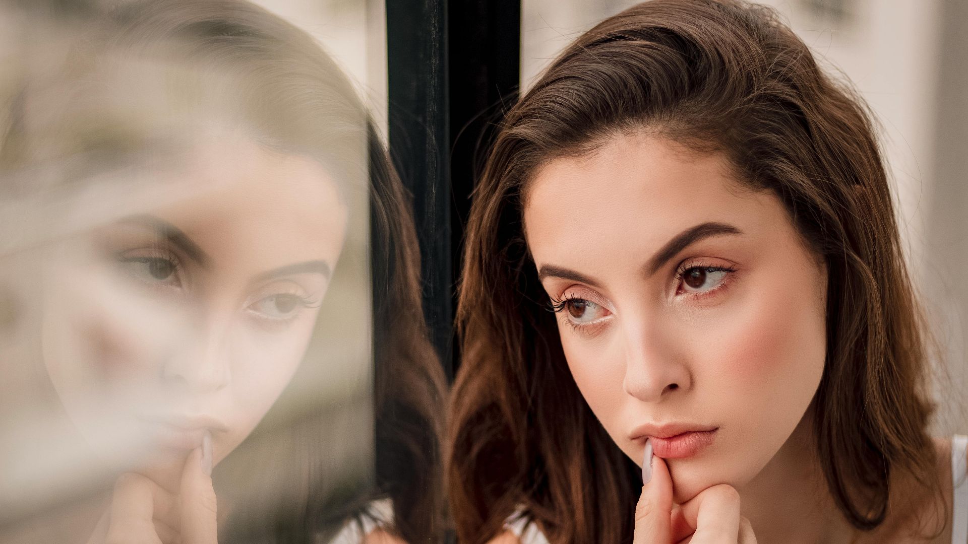 A pensive woman looks out a window, her reflection creating a thoughtful portrait.