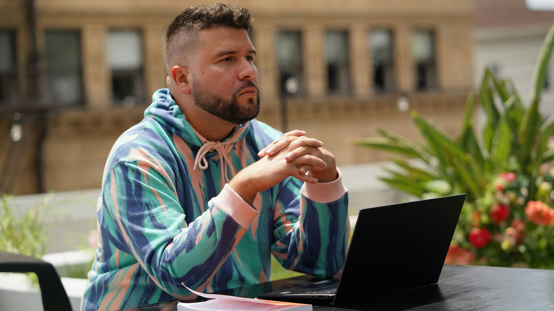 man in blue and white tribal print hoodie sitting beside black laptop computer