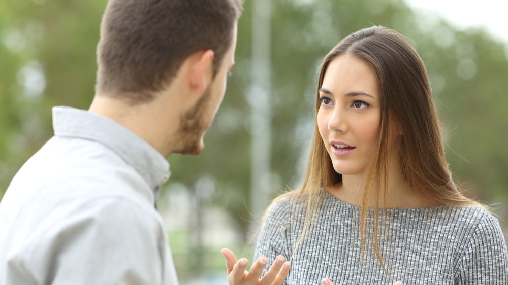 Couple talking outdoors in a park with a green background