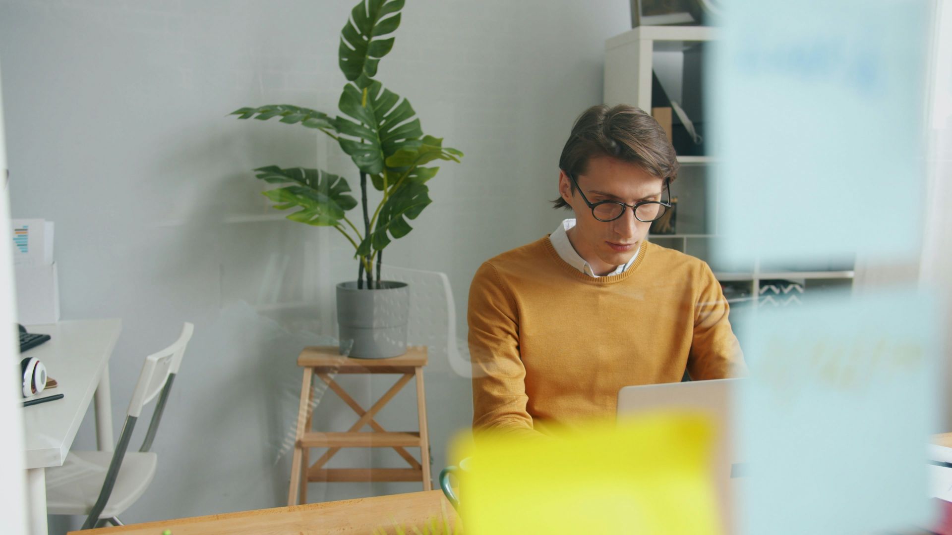 Man in glasses working on laptop in office.