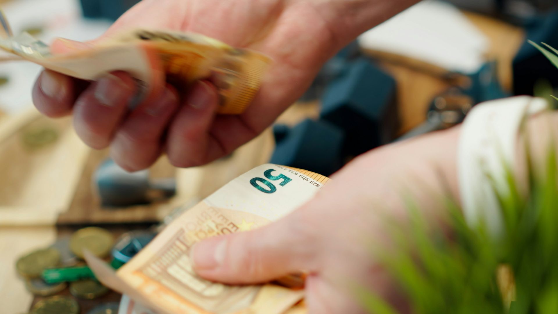 Hands counting euro banknotes with coins scattered around.