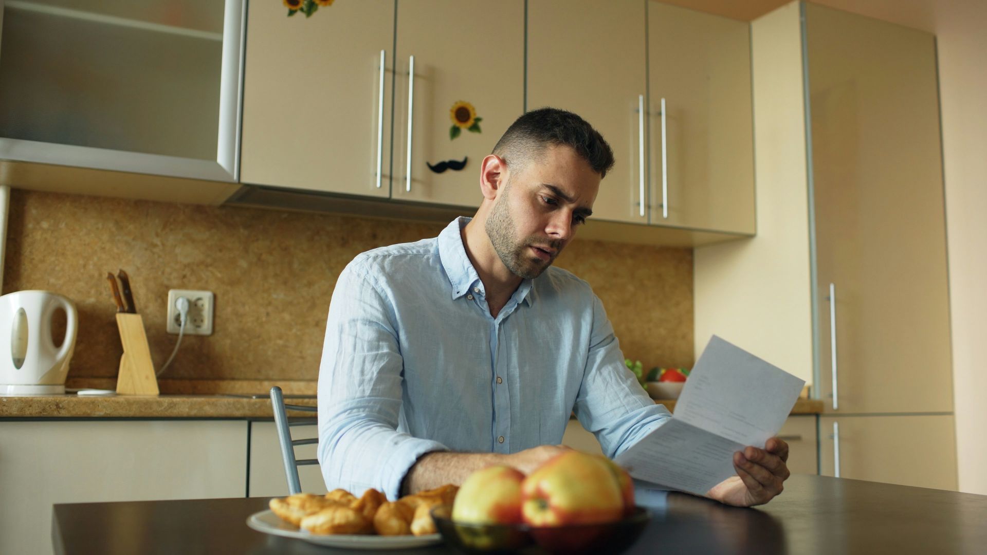 Man reading document at kitchen table with fruit and fruit