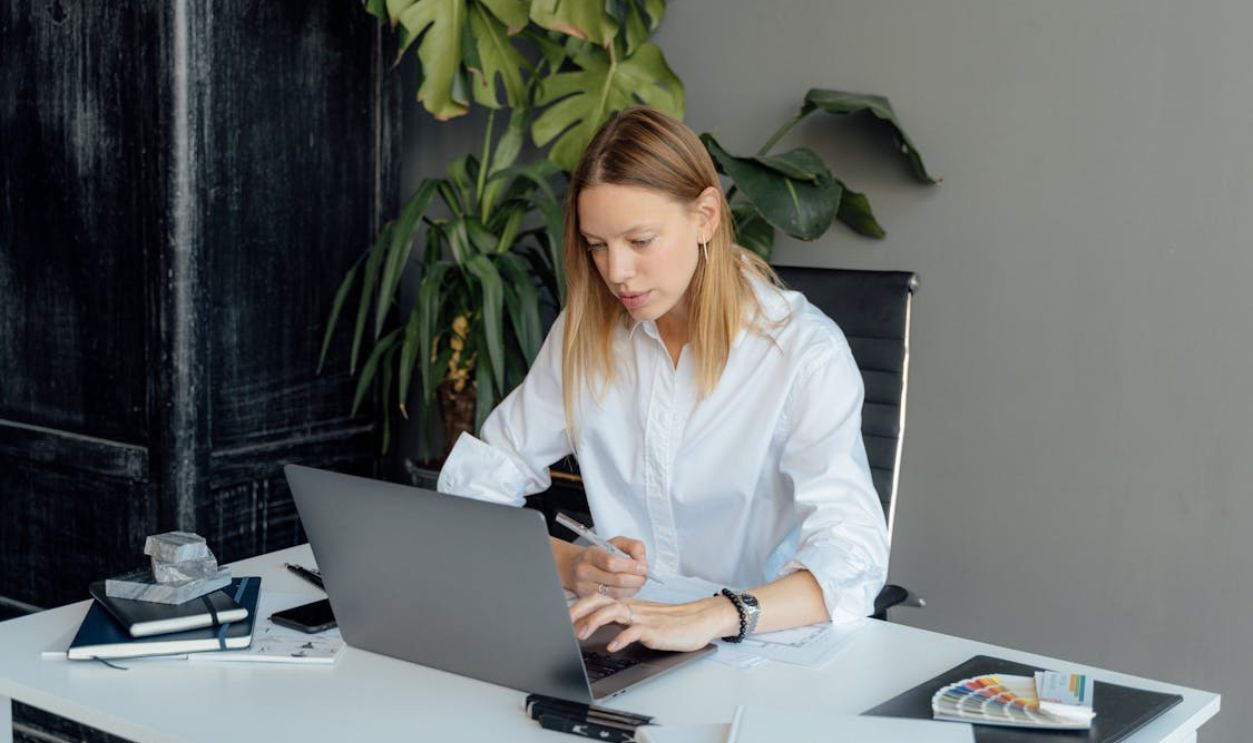 A Woman in White Long Sleeves Typing on Her Laptop