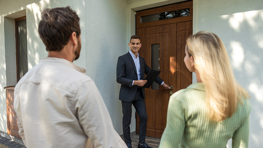 A realtor opens the door to show a house to a couple - seller