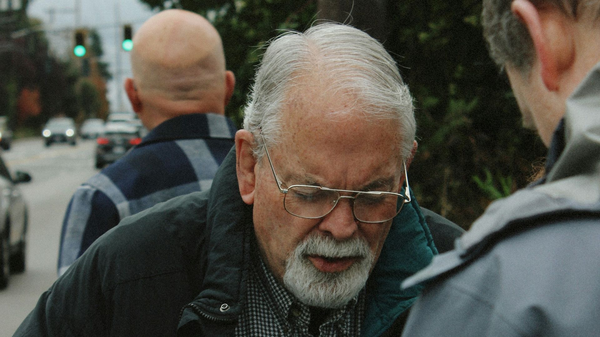 Elderly man holding a pamphlet with glasses and beard.