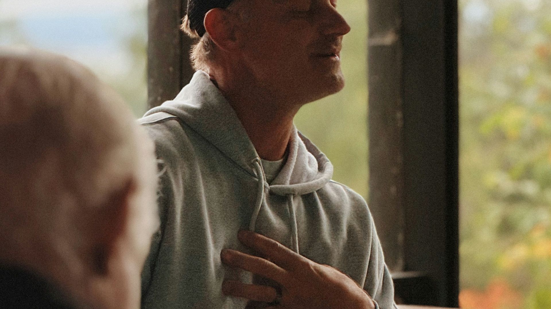 Man in baseball cap talking with hand on chest