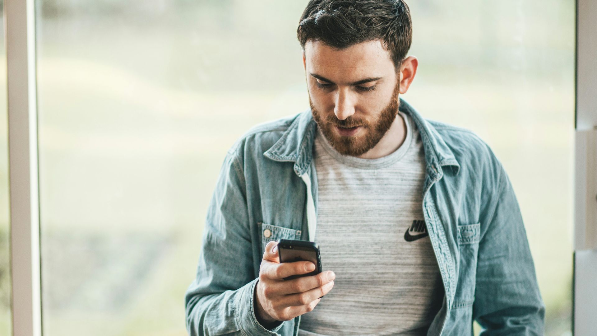 man holding a smartphone near the window