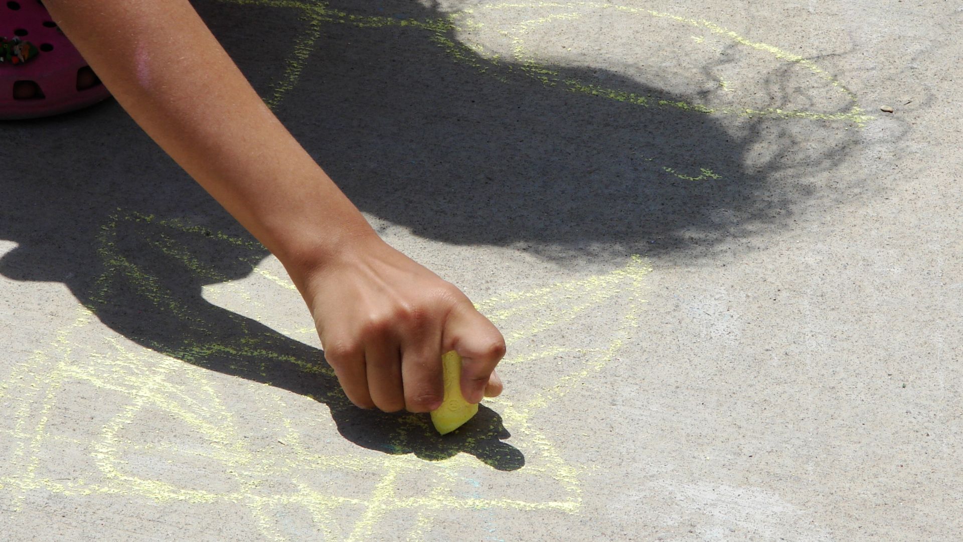Child creating sidewalk art using colored chalk.