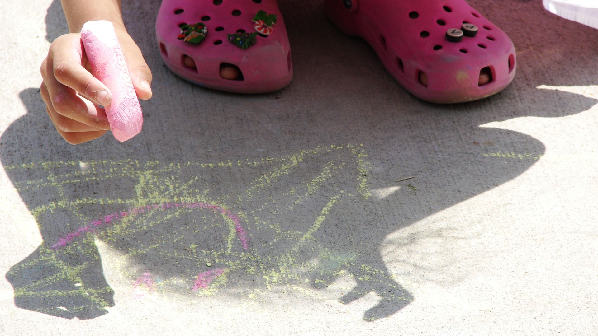 Child creating sidewalk art using colored chalk.