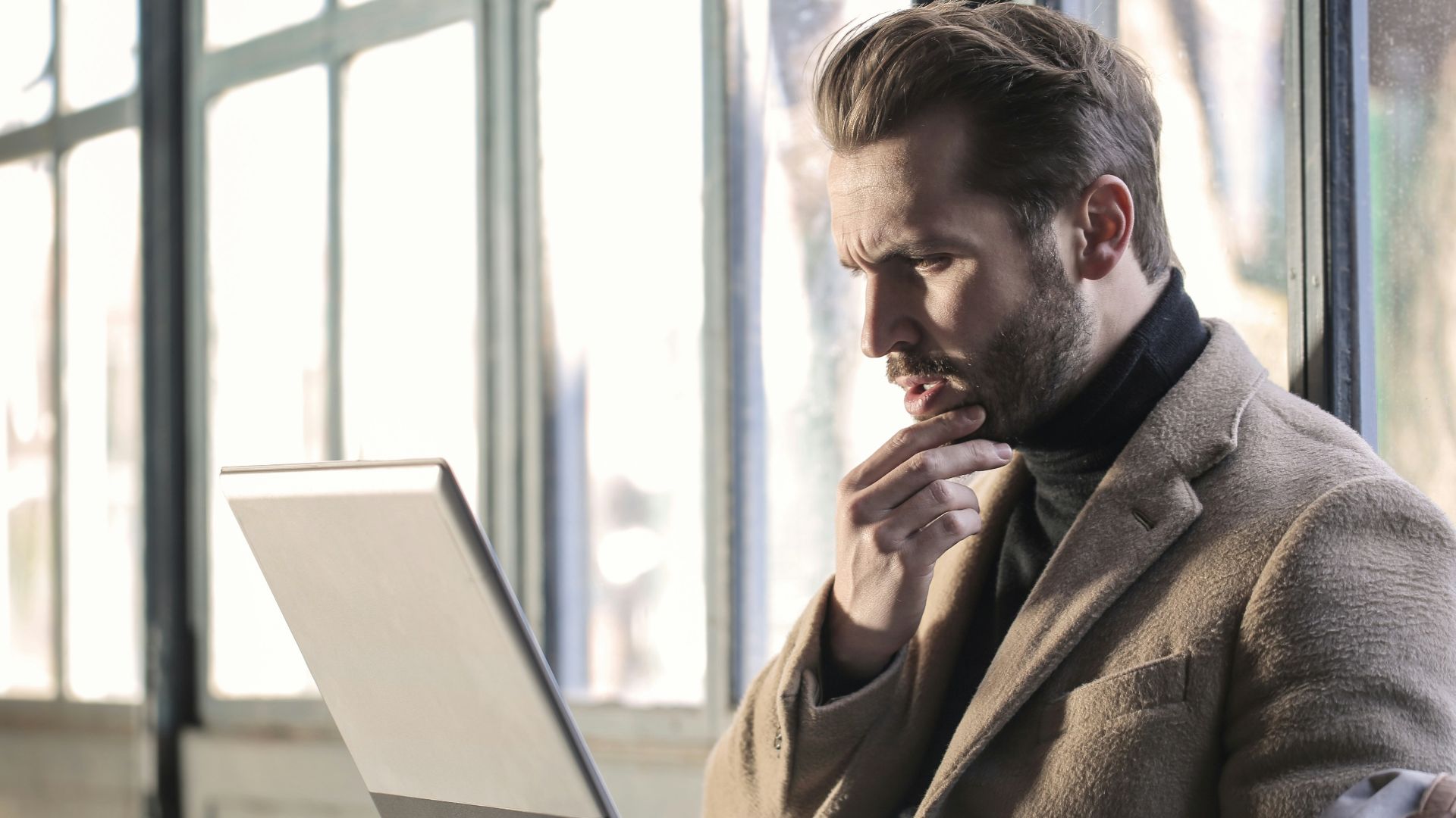 man holding his chin facing laptop computer