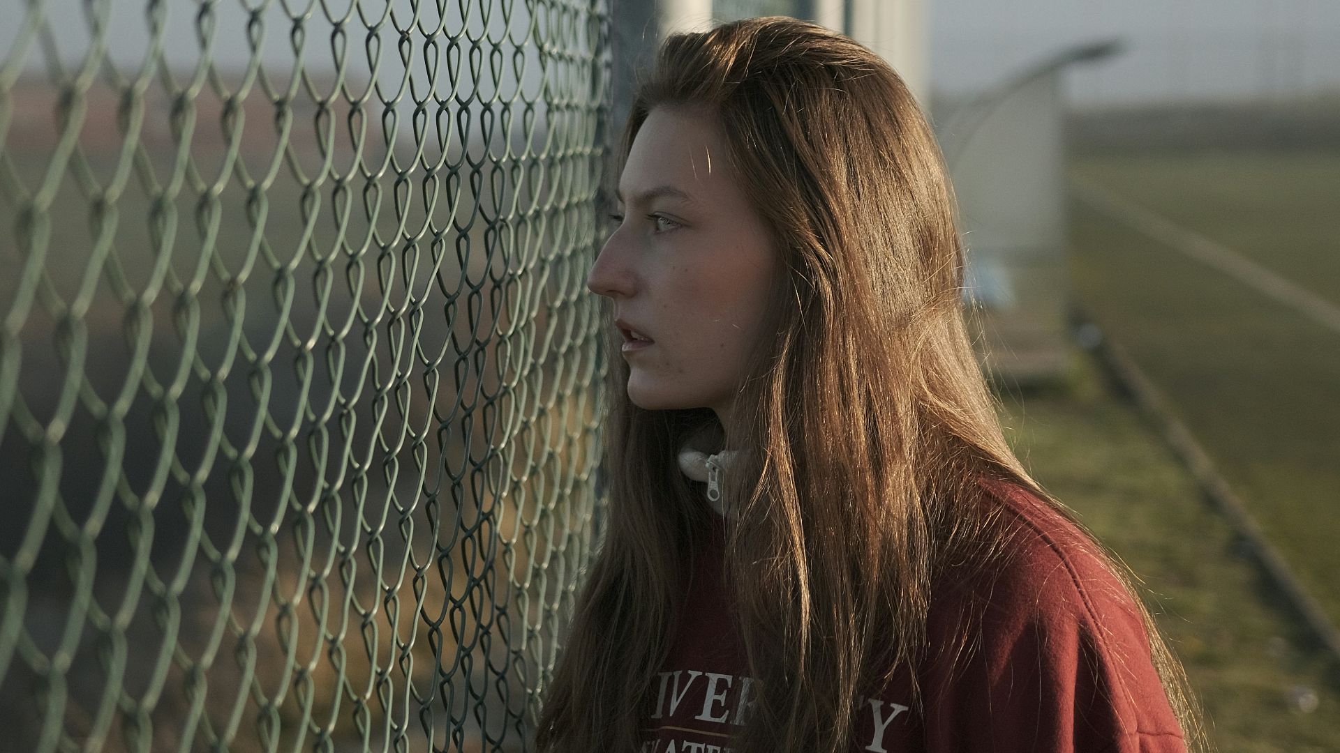 A young woman looks through a chain-link fence.