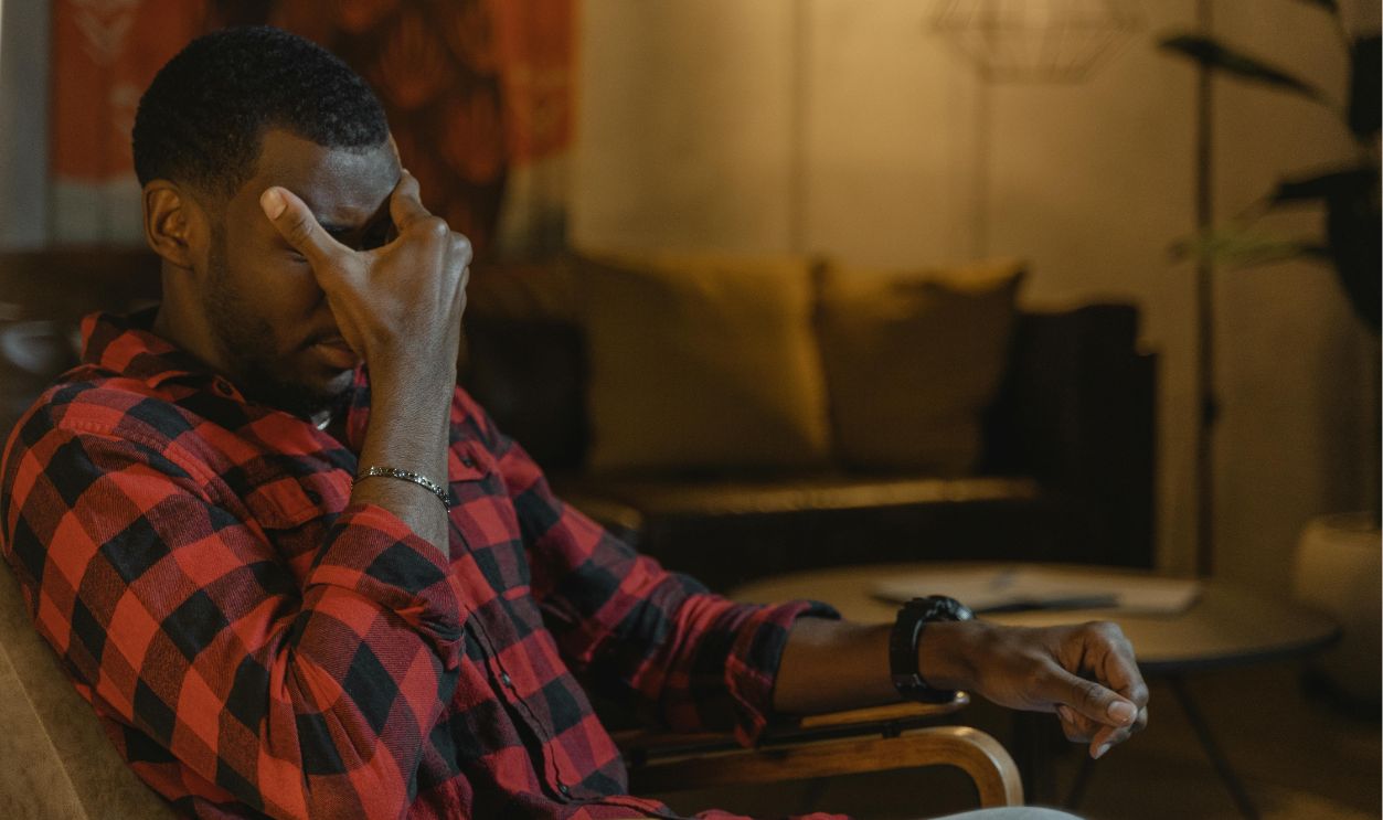 Man in Red Black and White Plaid Dress Shirt Sitting on Brown Wooden Armchair Feeling Exhausted