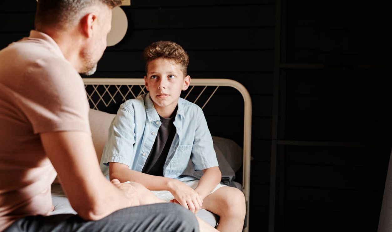 A Father and Son Talking while Sitting on a Bed