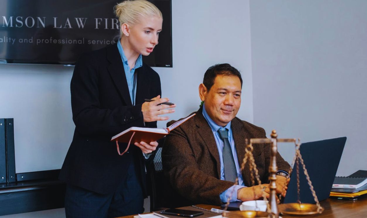 Ethnic male lawyer showing document on laptop to young female colleague