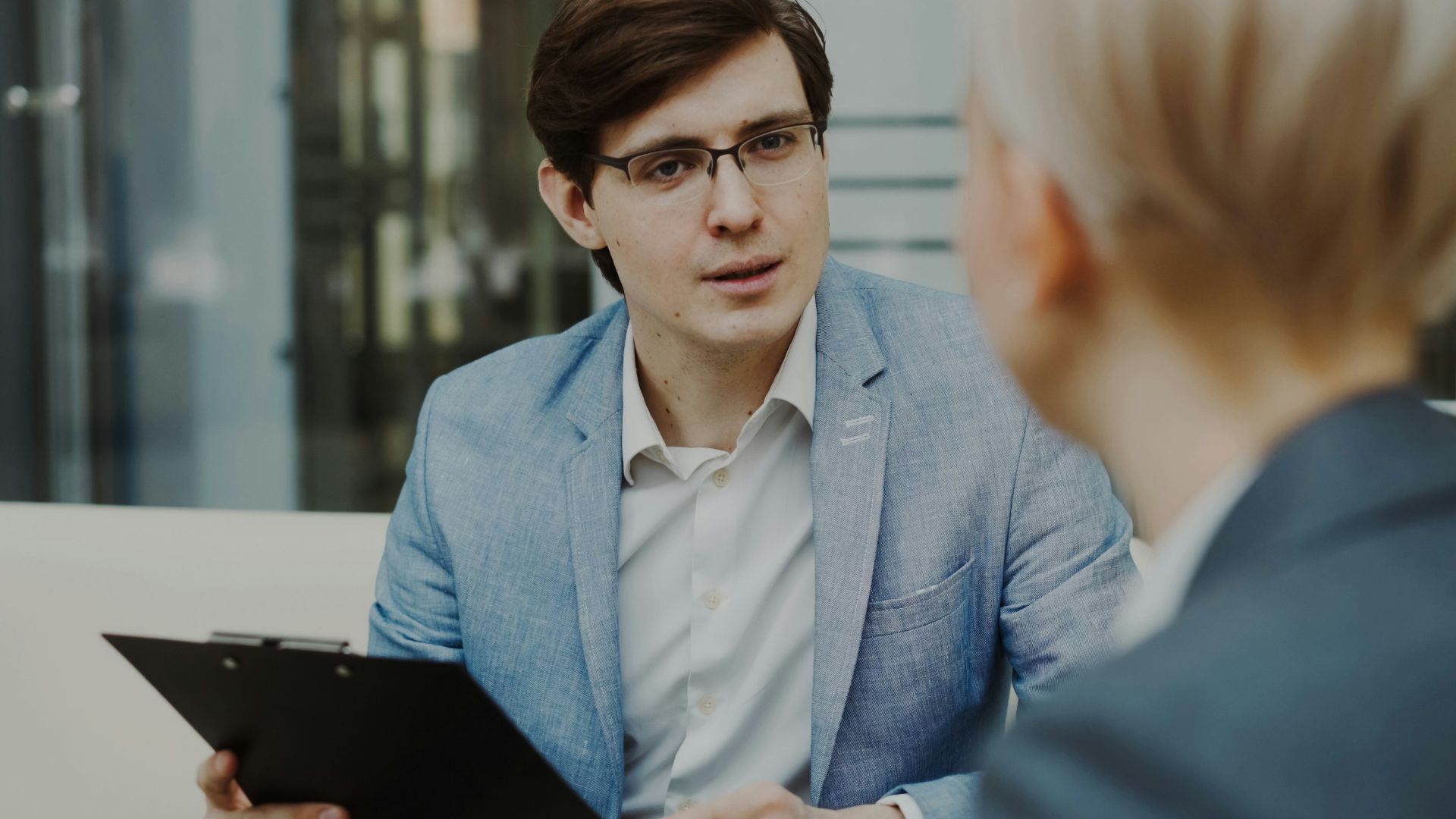 Man in suit holding clipboard talking to woman