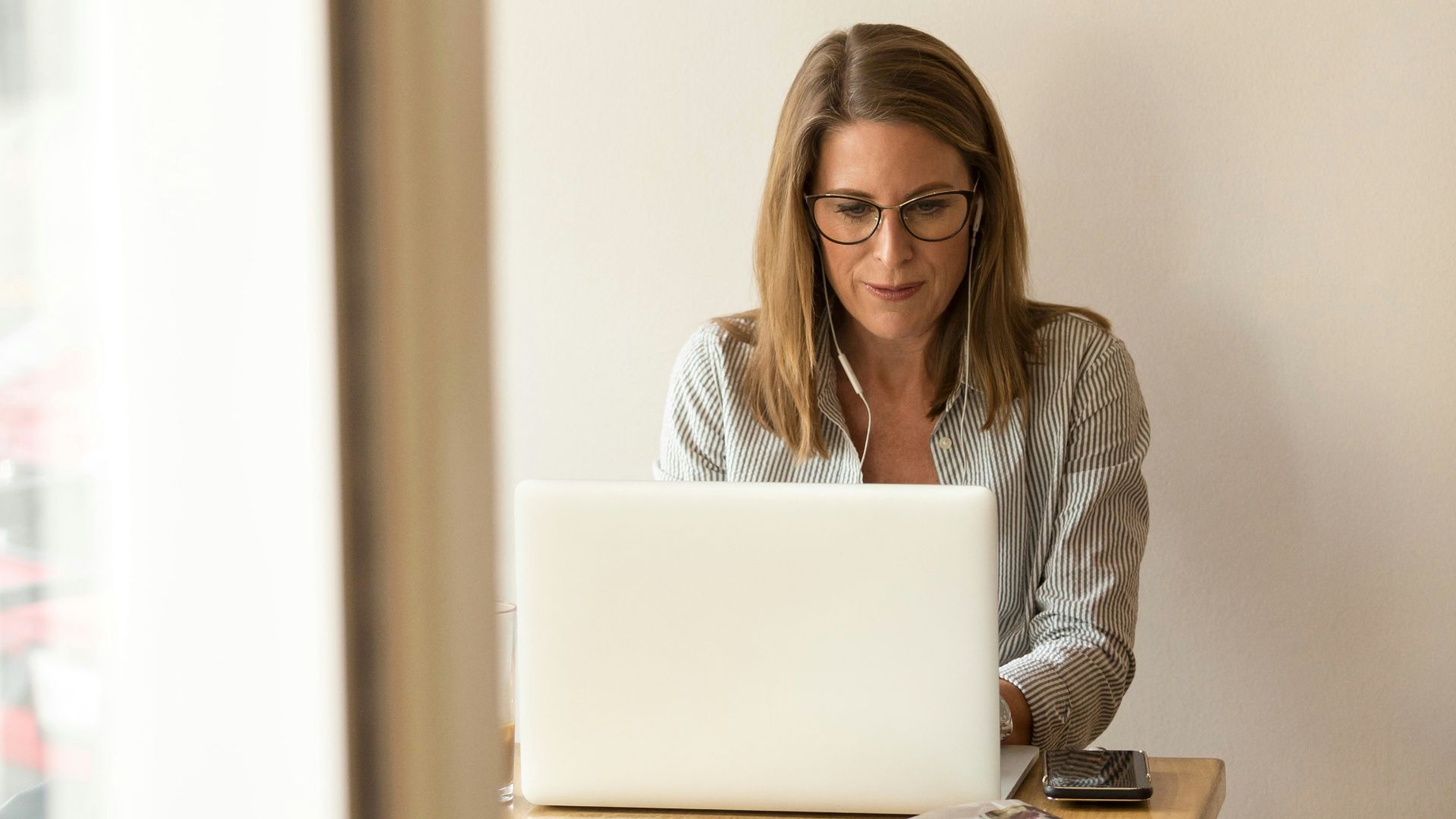 woman wearing grey striped dress shirt sitting down near brown wooden table in front of white laptop computer