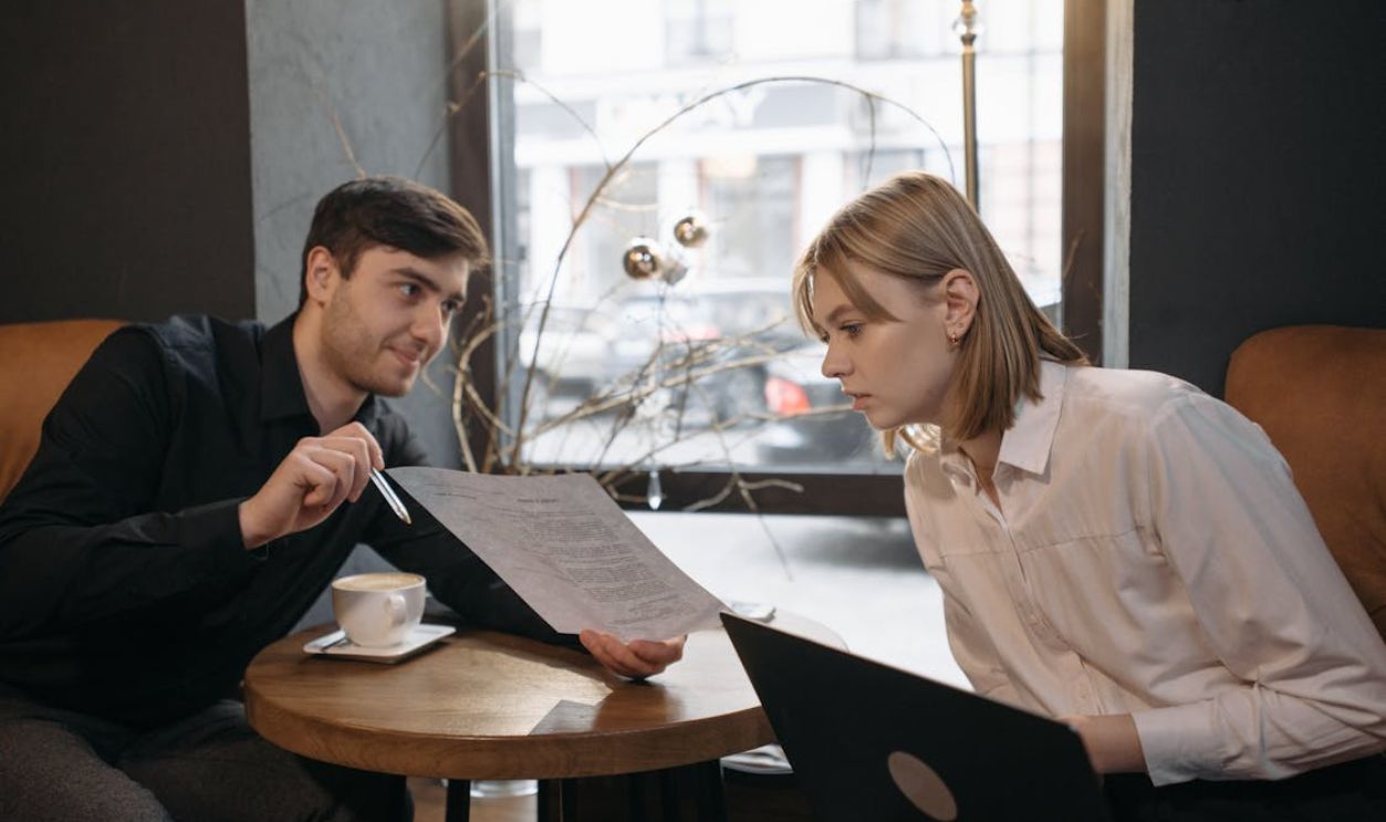 A Man Showing a Paper to a Woman Sitting Across