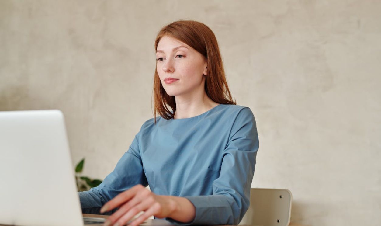Woman in Blue Long Sleeve Shirt Using a Silver Macbook