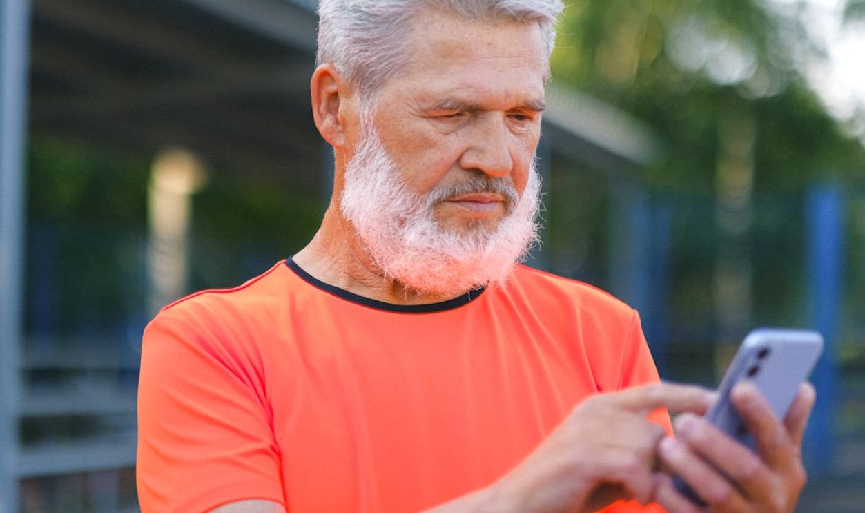 Elderly man with beard and gray hair using a smartphone in a park setting