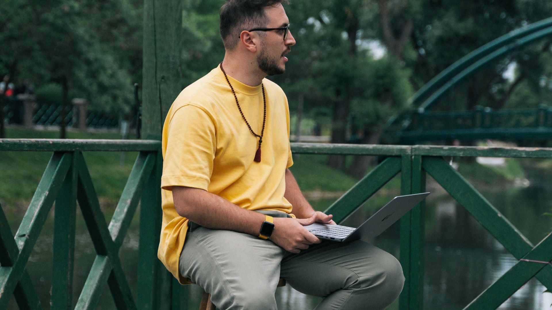A man using a laptop seated by a riverside, blending nature with technology.